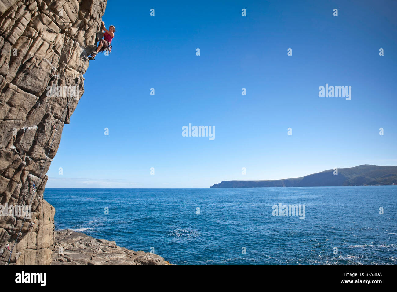 Una donna è la scalata di un rockface sulla Penisola Tasmana, Tasmania, Australia. Foto Stock
