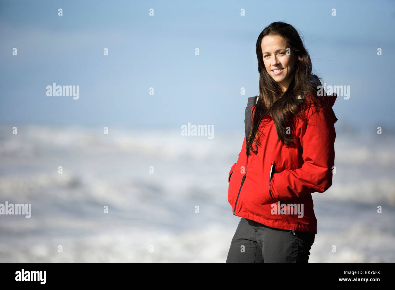 Una donna che sorride alla telecamera mentre guardando le onde del mare in un mare turbolento. Foto Stock
