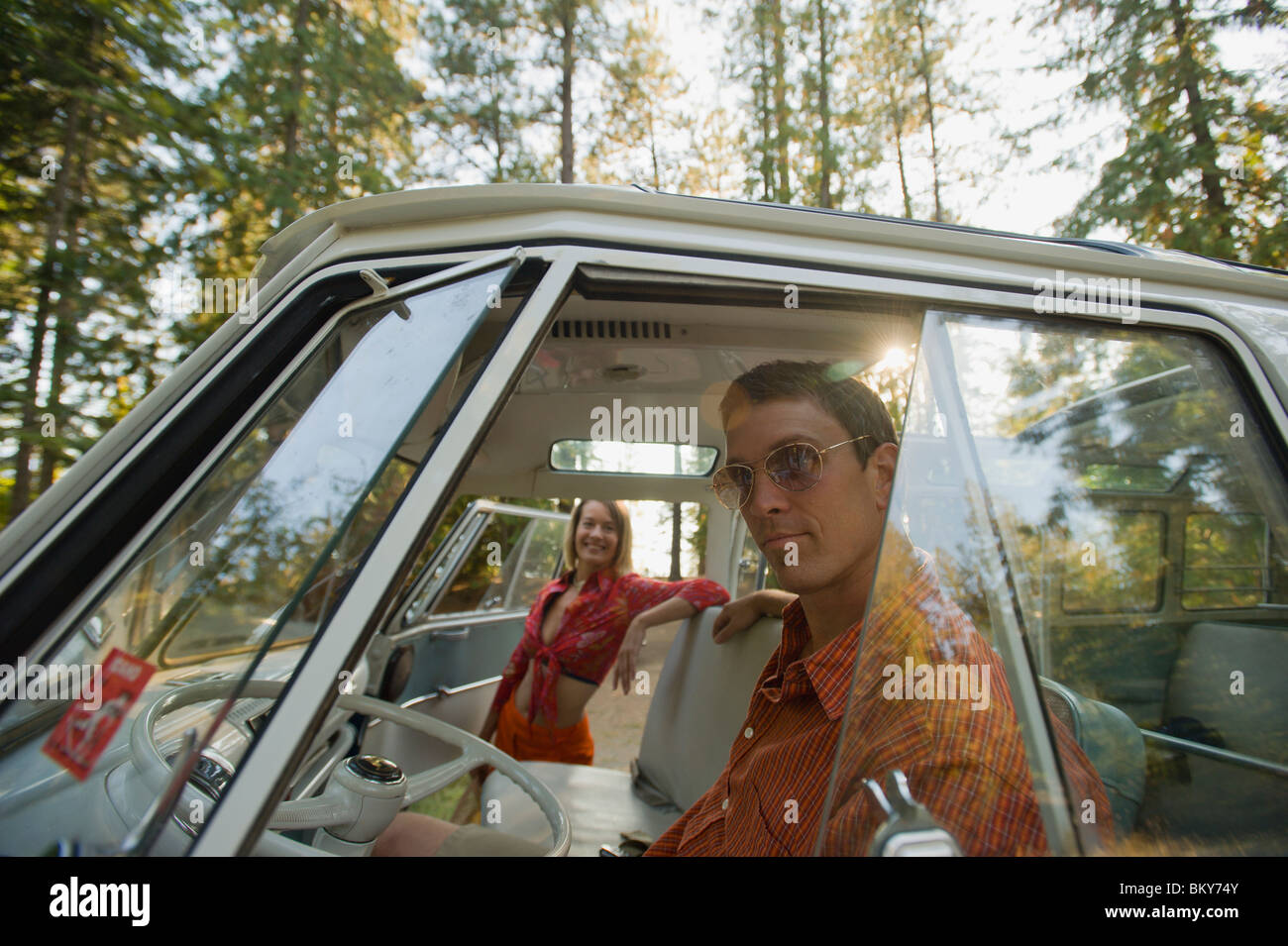 Un giovane uomo in occhiali da sole offre una donna un giro in un furgone vintage. Foto Stock