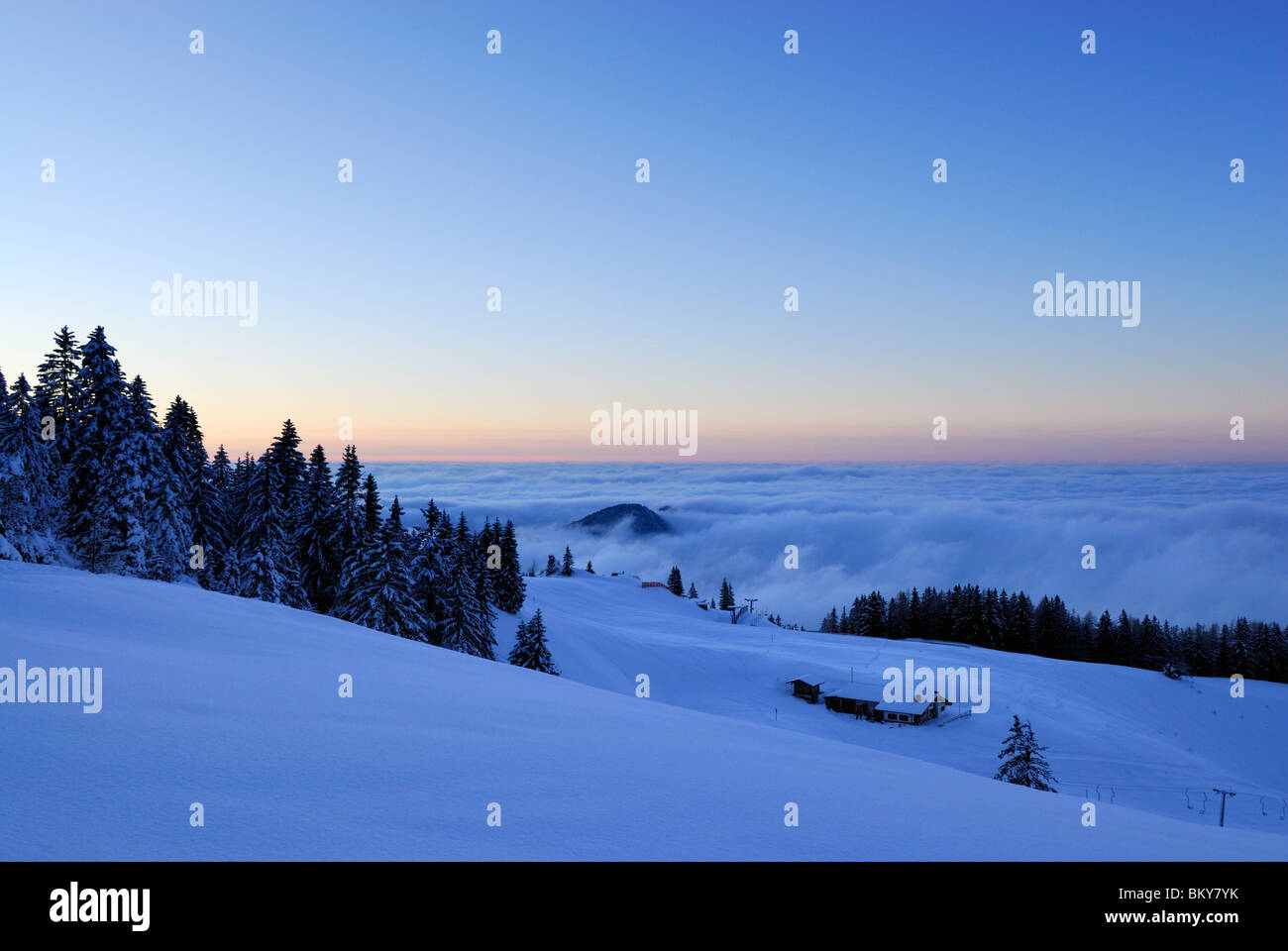 Coperte di neve rifugio alpino sopra banco di nebbia al tramonto, Kampenwand, Chiemgau Alpi, Chiemgau, Baviera, Germania Foto Stock