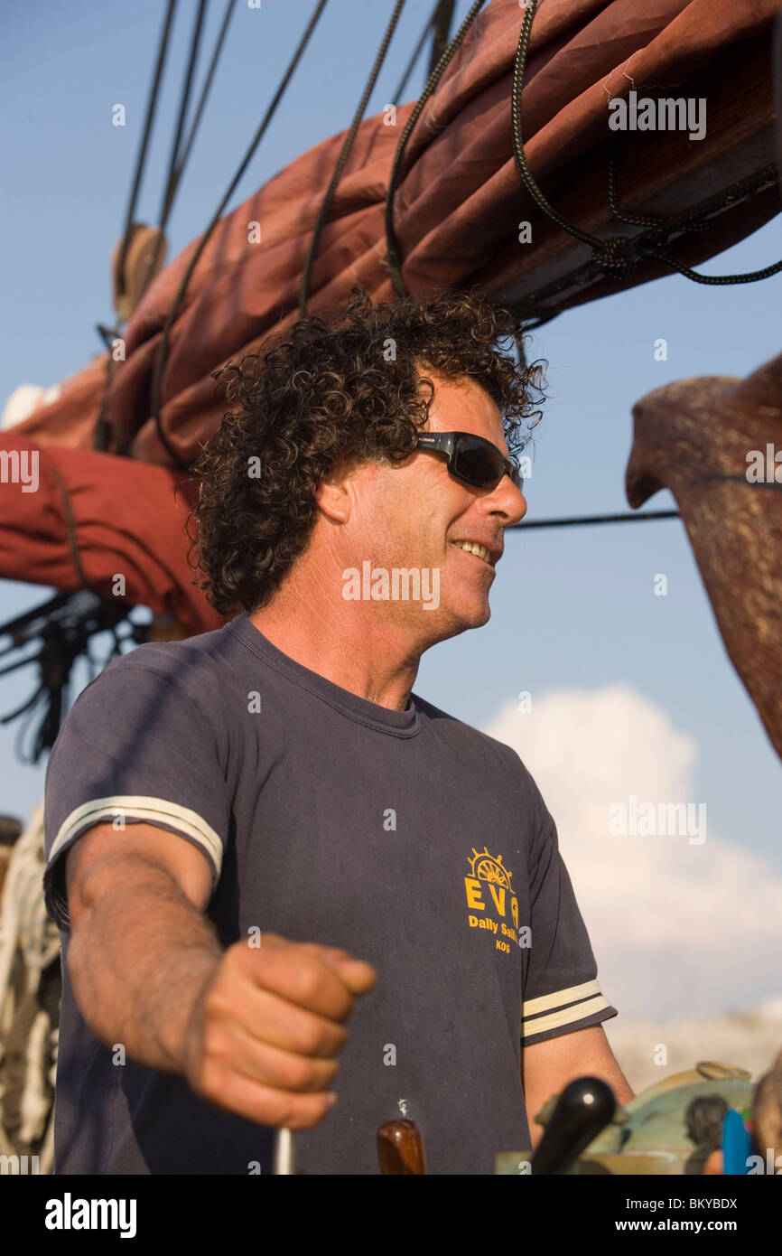 Il capitano in piedi sulla ruota di una imbarcazione a vela durante un viaggio in barca a baia a Kalymnos, Grecia Foto Stock