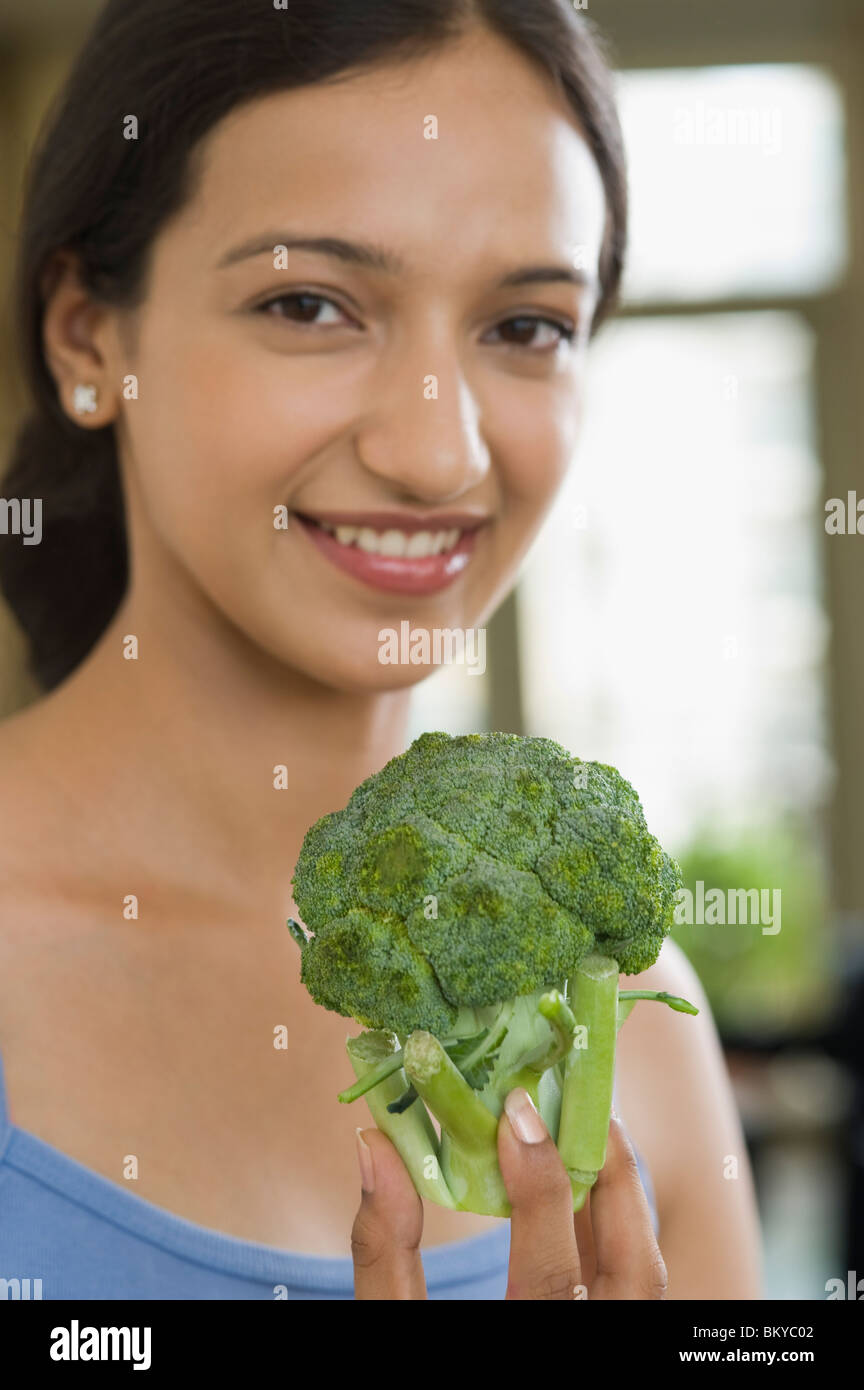 Donna che mantiene un broccoli e sorridente Foto Stock