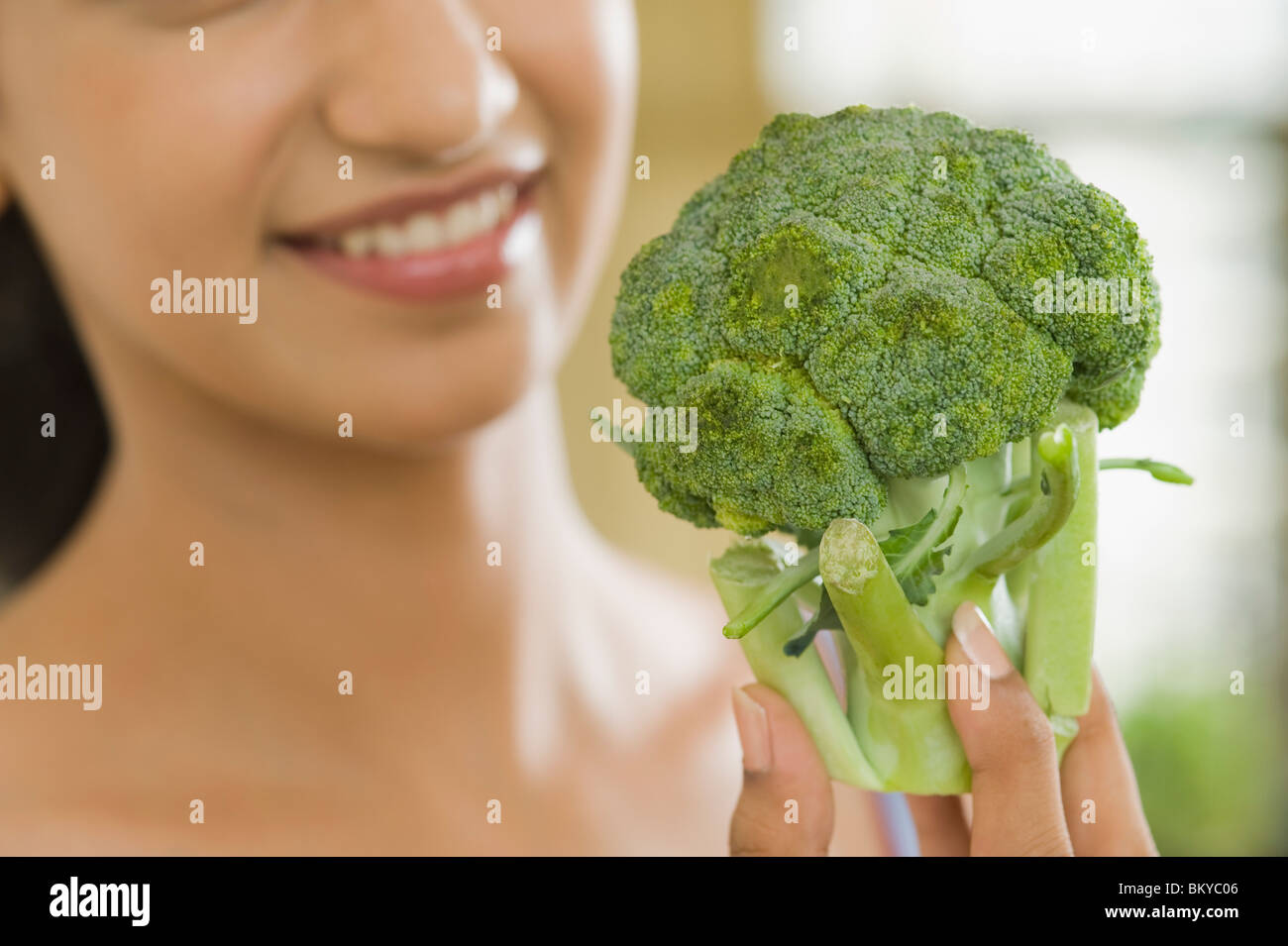 Donna che mantiene un broccoli e sorridente Foto Stock