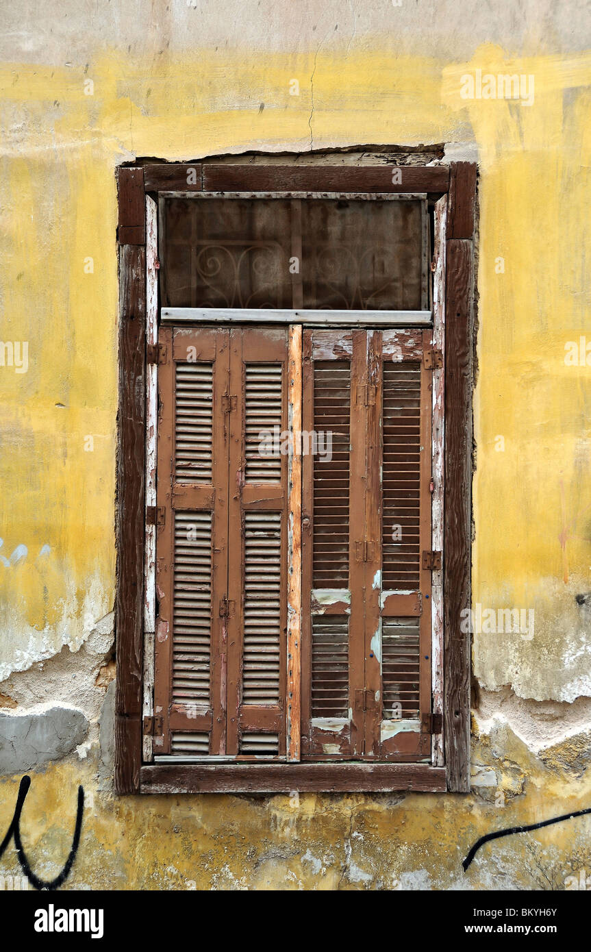 Intavolato persiane alle finestre e grungy parete gialla. Casa abbandonata dettaglio. Foto Stock