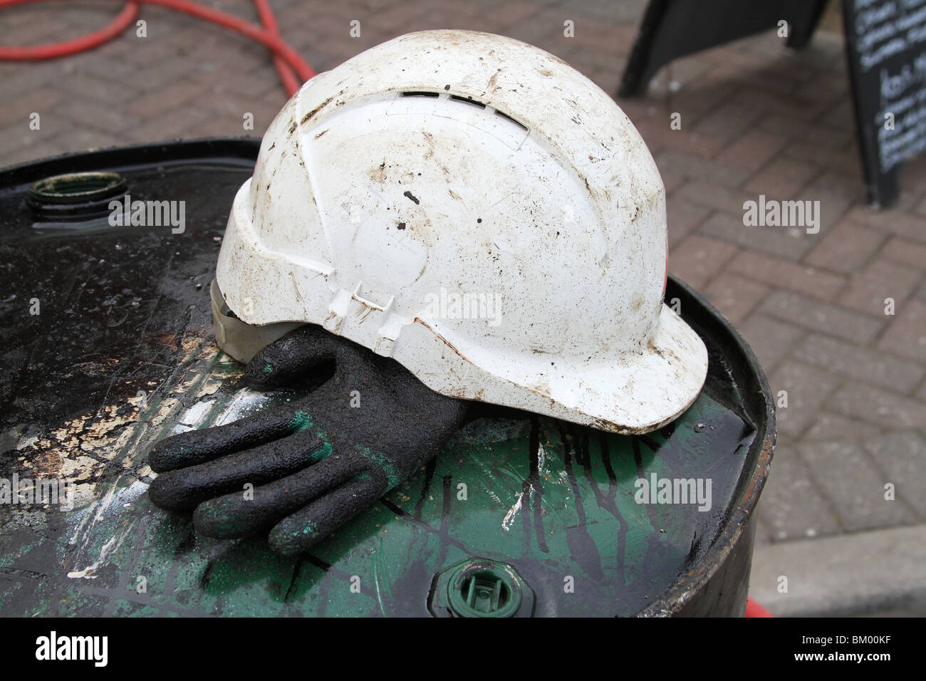 Bianco casco di sicurezza e gravemente inquinato guanto sulla canna di catrame. Foto Stock