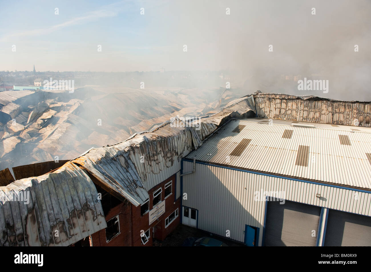 Grande fabbrica e magazzino collassato e a covare dopo un grave incendio notte prima - Vigili del Fuoco basso smorzamento Foto Stock
