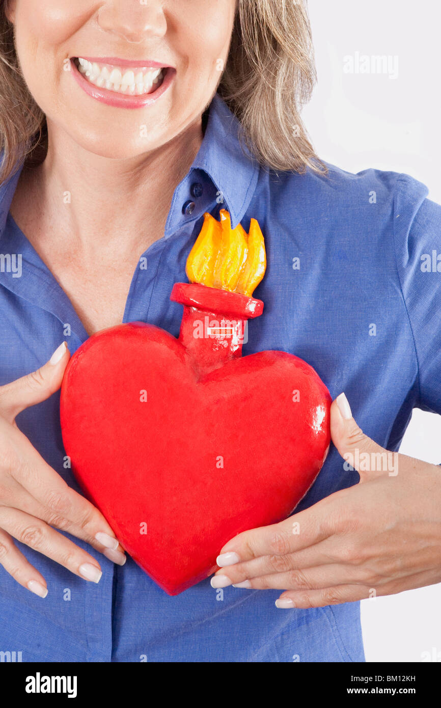 Donna che mantiene artificialmente un cuore in fiamme contro il suo torace e sorridente Foto Stock