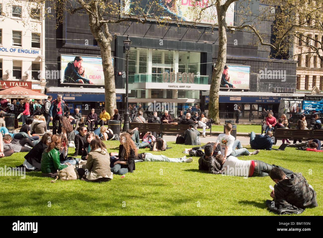 Gli adolescenti seduto sull'erba godendo il sole, Leicester Square, London REGNO UNITO Foto Stock