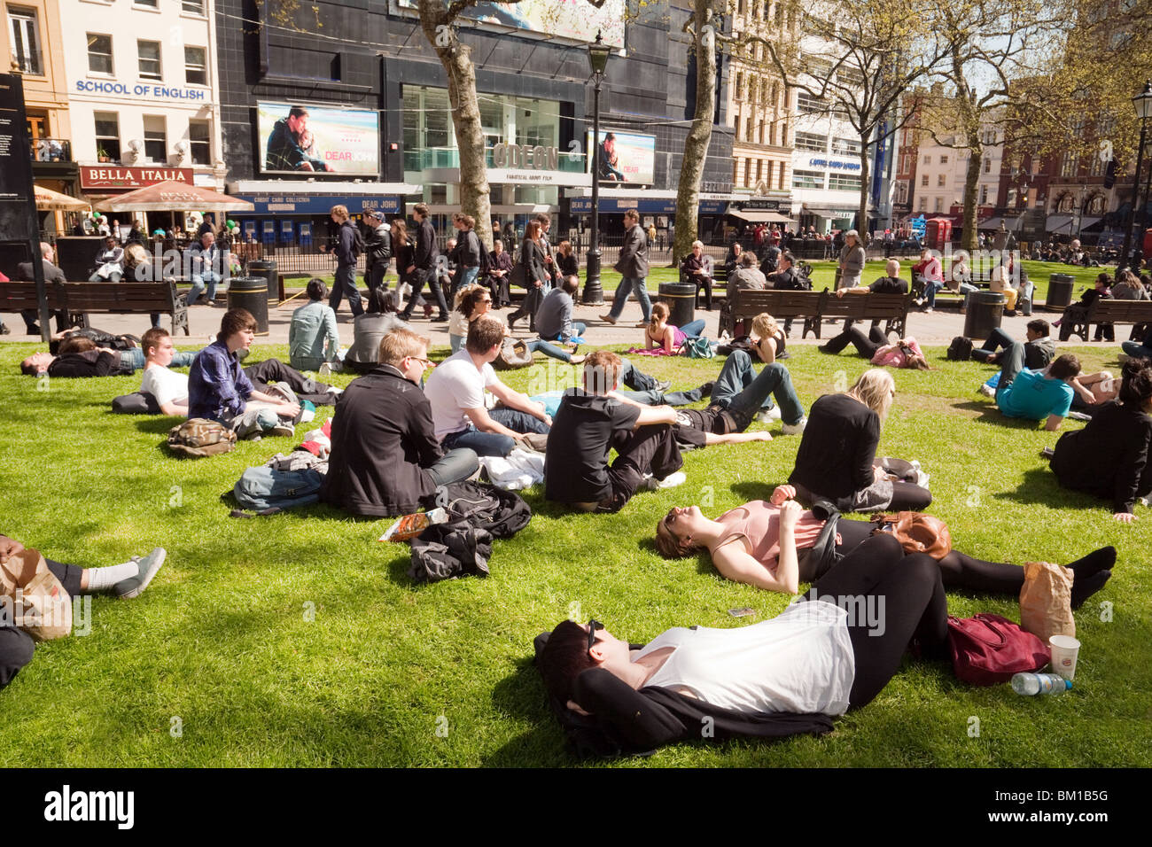 Gli adolescenti seduto sull'erba godendo il sole, Leicester Square, London REGNO UNITO Foto Stock