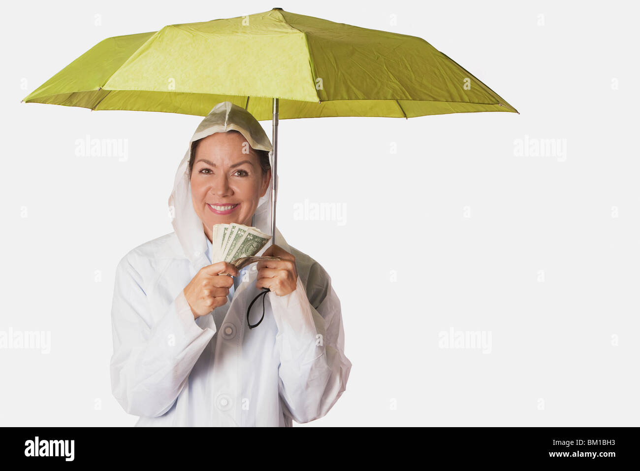 Donna in cappotto di pioggia il ricovero sotto un ombrello e tenendo moneta note Foto Stock