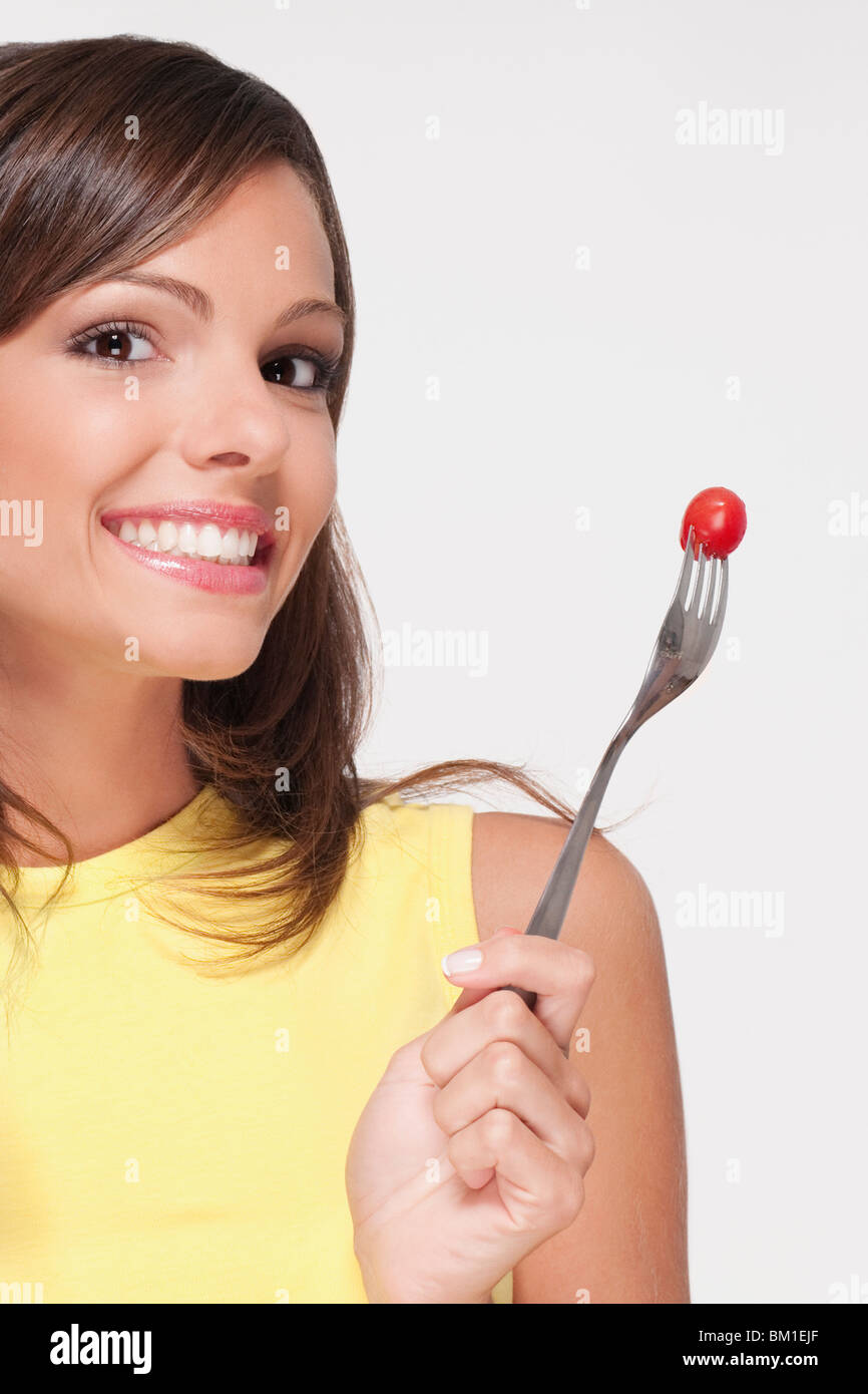 Ritratto di una donna tenendo un pomodoro ciliegino su una forcella Foto Stock