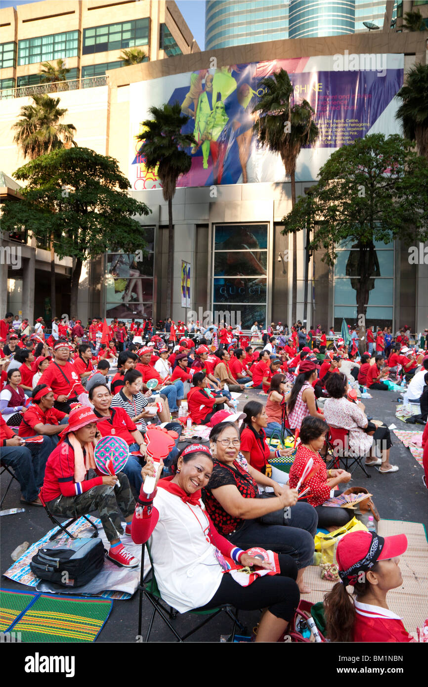 Felice rosso-shirted manifestanti sedersi in strada dominata dalla chiusa di grandi magazzini. Foto Stock