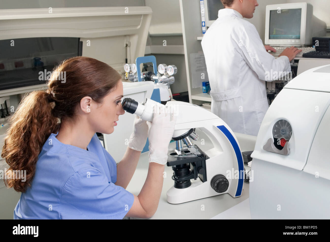 Femmina tecnico di laboratorio di analisi di un campione attraverso un microscopio Foto Stock
