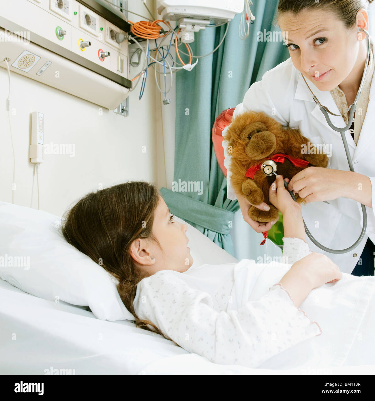 Ragazza sul letto di un ospedale con un medico donna esaminando un giocattolo imbottito Foto Stock
