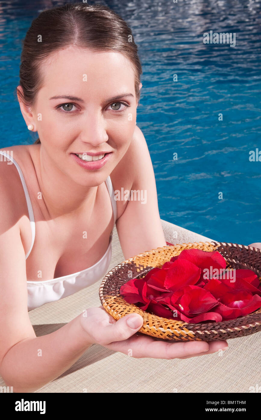 Donna che mantiene un piatto di petali di rosa a bordo piscina Foto Stock