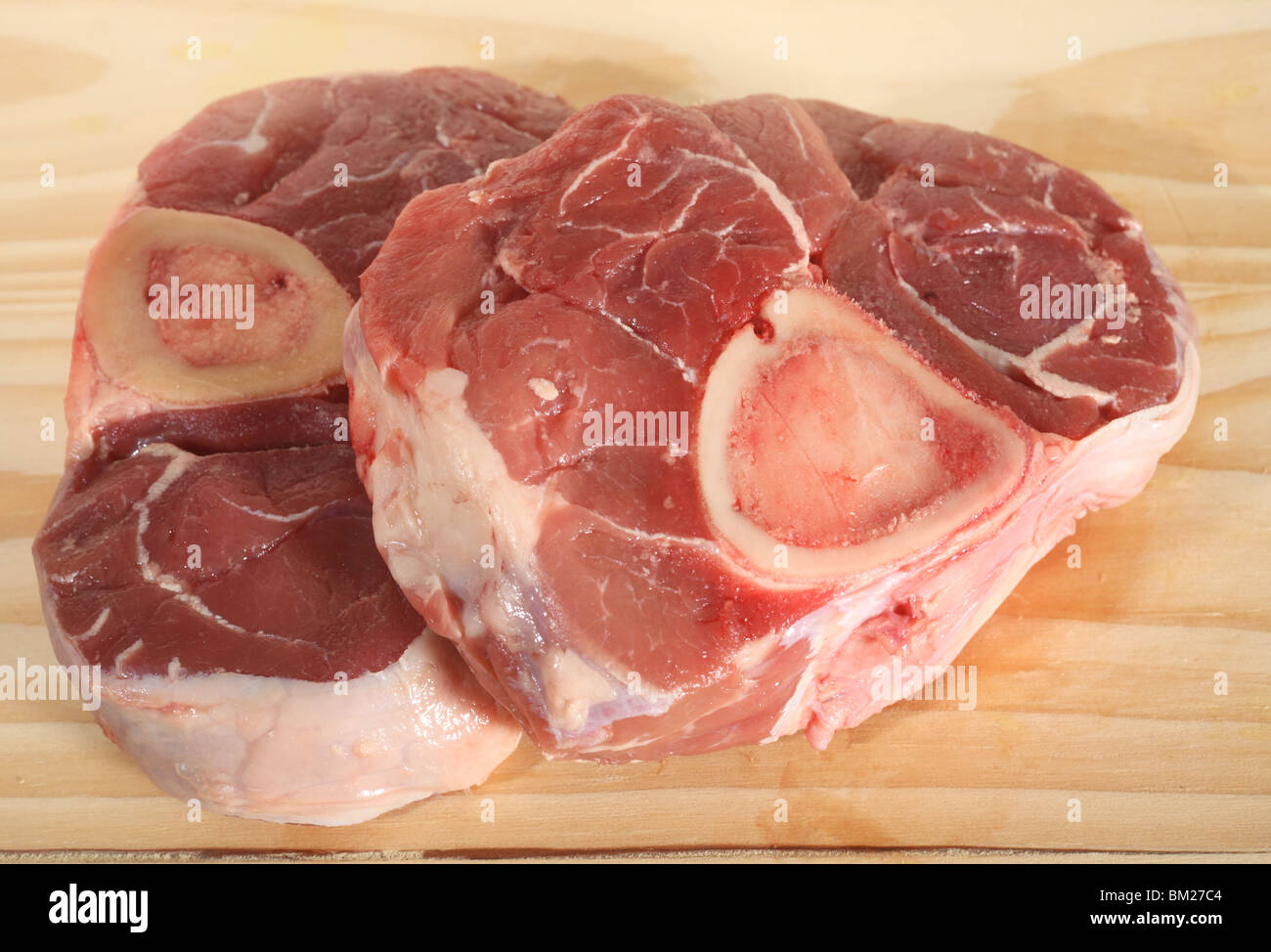 Due pezzi di ossobuco (carni di agnello bistecche di gambo) su un tagliere di legno Foto Stock