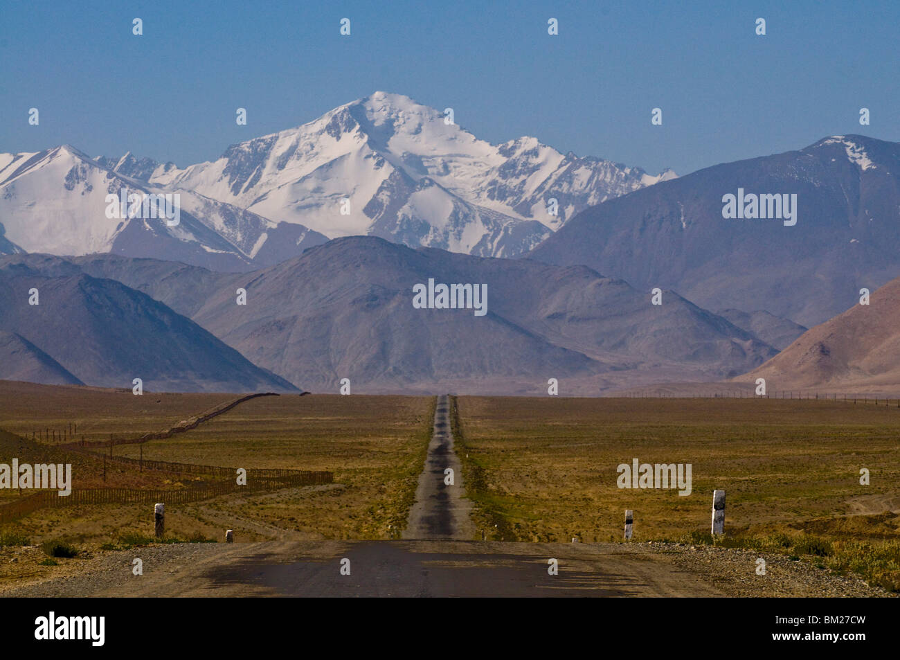 Paese strada che conduce alle montagne coperte di neve, Karakul, in Tagikistan, in Asia centrale Foto Stock