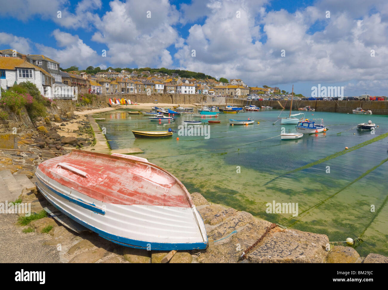 Piccola imbarcazione non ruotata sulla banchina e piccole barche nel porto racchiuso a Mousehole, Cornwall, Regno Unito Foto Stock