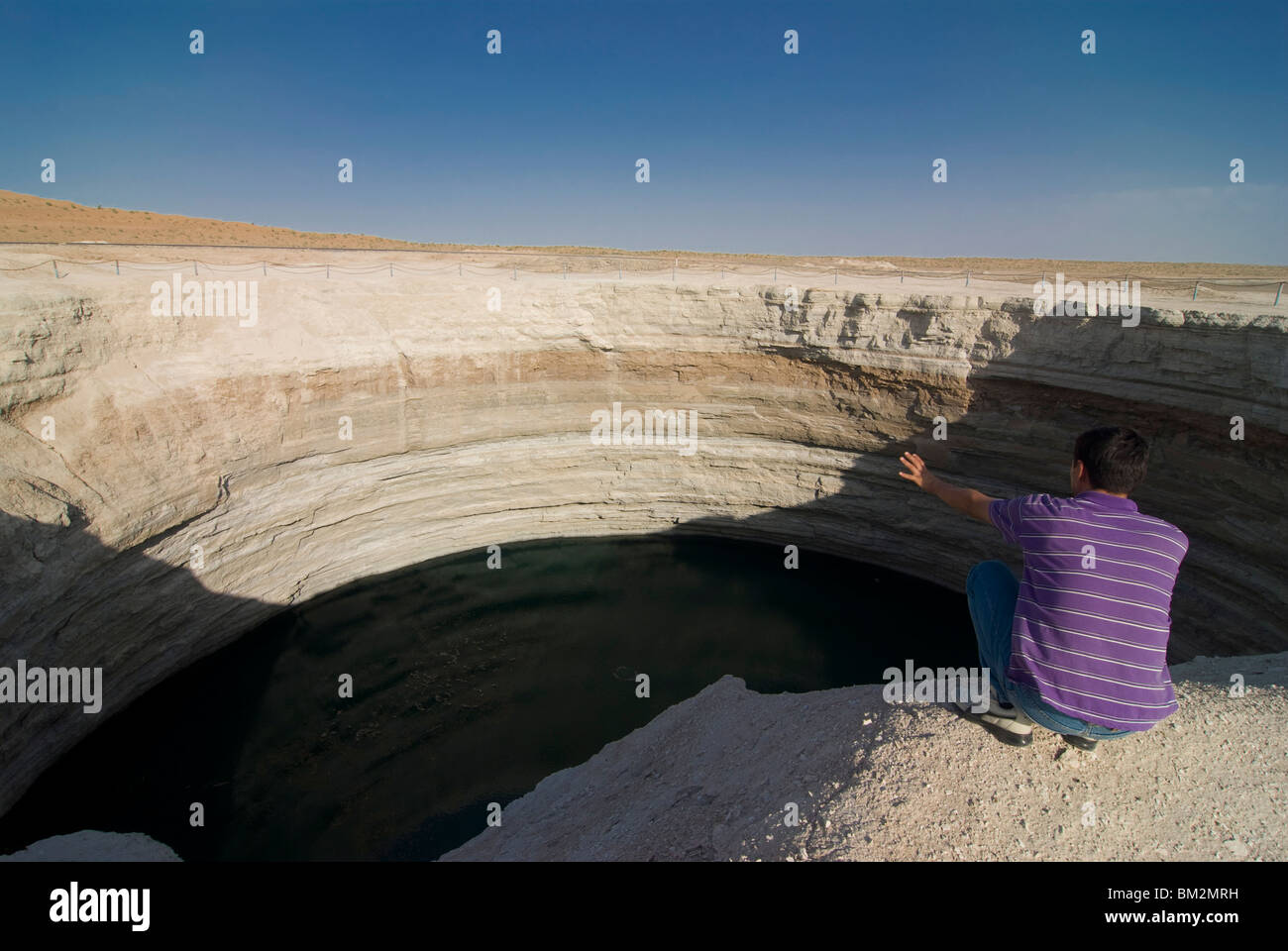 Uomo seduto sulla cima di un cratere riempito con acqua, Karakol deserto, Turkmenistan Foto Stock