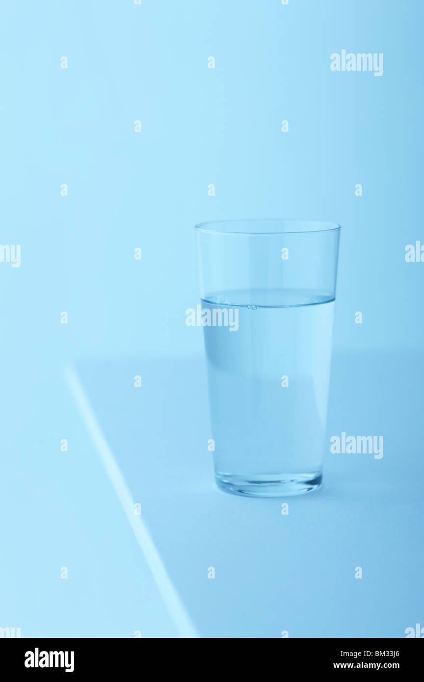 Bicchiere di acqua sul tavolo, sfondo blu, soft focus Foto Stock