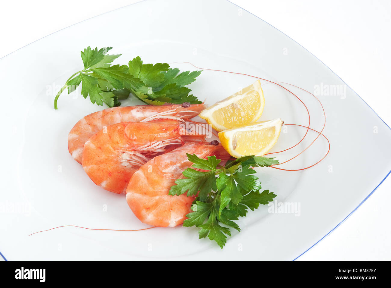 Tre materie di gamberi con limone e prezzemolo su una piastra bianca isolata con tracciato di ritaglio Foto Stock