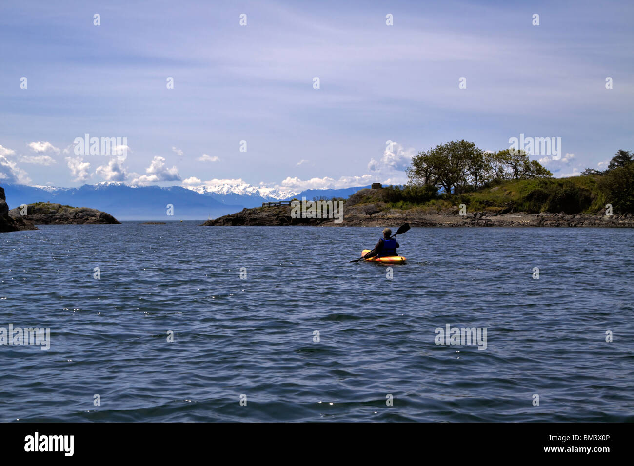 Un kayaker pale verso il 18 miglio distanti montagne olimpiche in Medio Harbour, Victoria, British Columbia, Canada Foto Stock