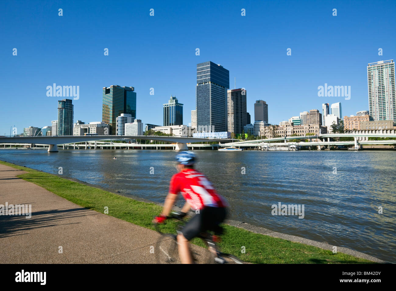Ciclista sul lungofiume al South Bank con lo skyline della città in background. South Bank, Brisbane, Queensland, Australia Foto Stock
