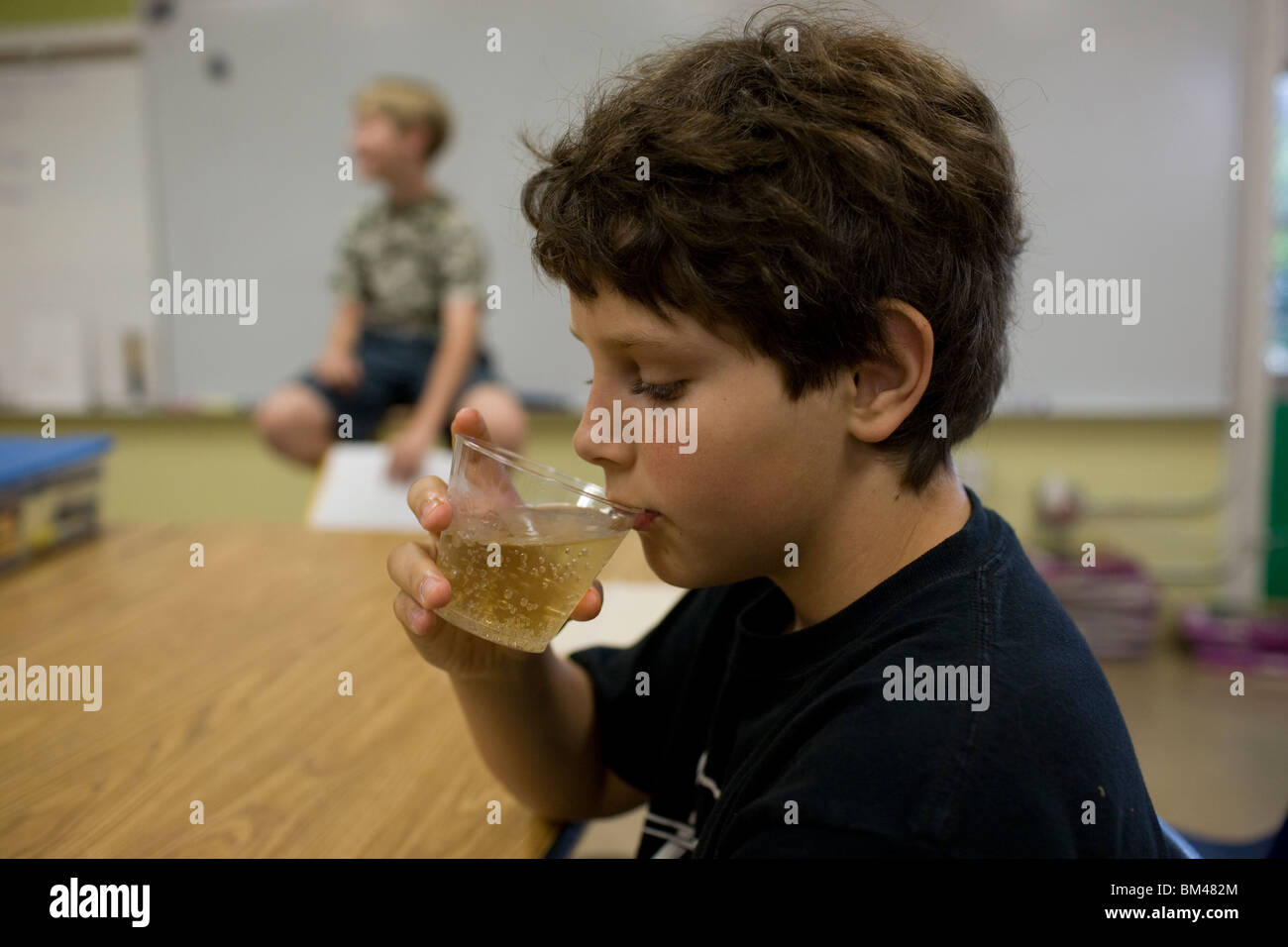 11-anno-vecchio ragazzo Anglo sips ginger ale da un bicchiere di plastica in corrispondenza di una parte della scuola. Foto Stock