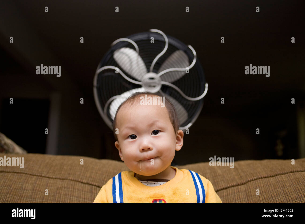 Asian baby boy seduti nella parte anteriore del ventilatore elettrico Foto Stock
