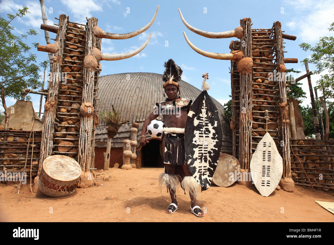 Un uomo tribali di origine Zulu indossa abbigliamento tradizionale mentre si pone con un pallone da calcio in un tradizionale villaggio in Sud Africa Foto Stock