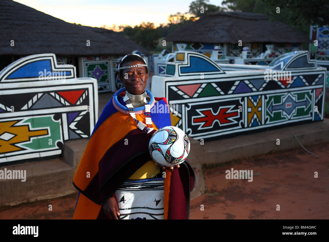 Una donna con i tradizionali tribù Ndebele colori stand con un pallone da calcio in un villaggio culturale a Mpumalanga, Sud Africa Foto Stock