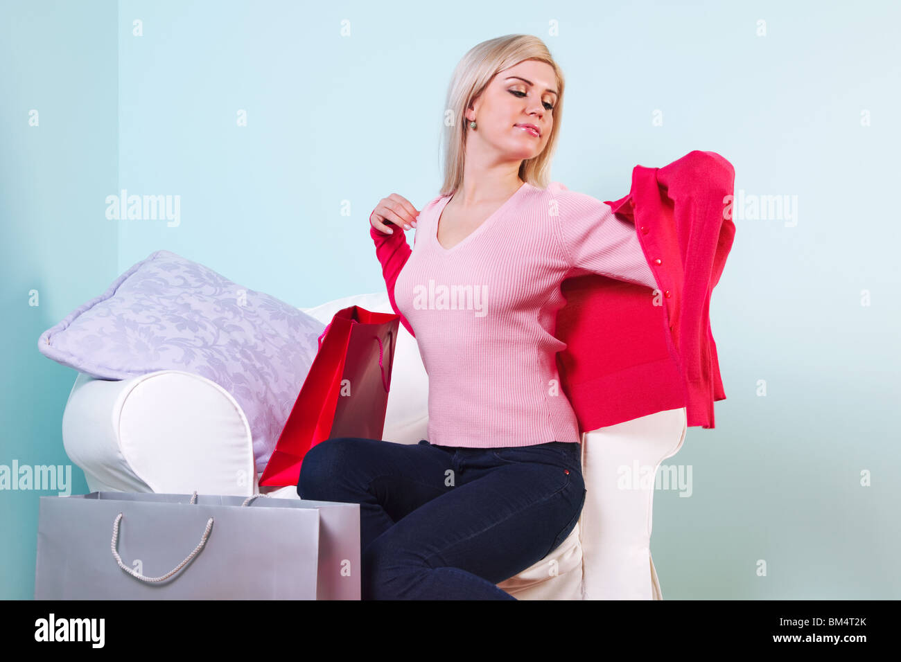 Un attraente donna bionda seduto in una sedia cercando su alcuni nuovi vestiti che ha appena acquistato. Foto Stock