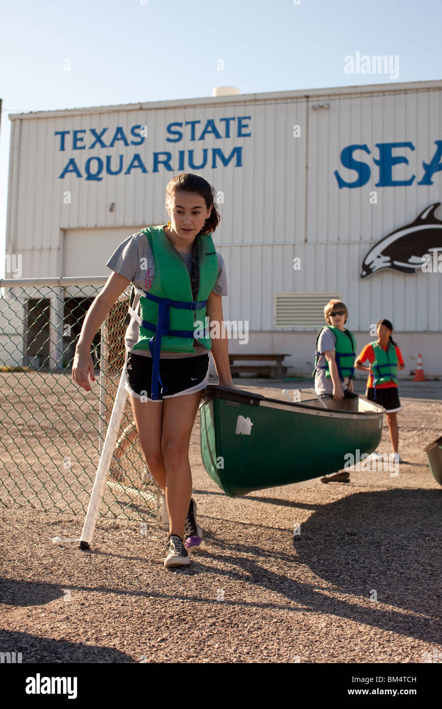 La scuola media di ragazzo e una ragazza portare canoe verso l'acqua durante il corso di studi di biologia marina di campo classe di viaggio a Corpus Christi Bay nel Corpus Christi TX. Foto Stock