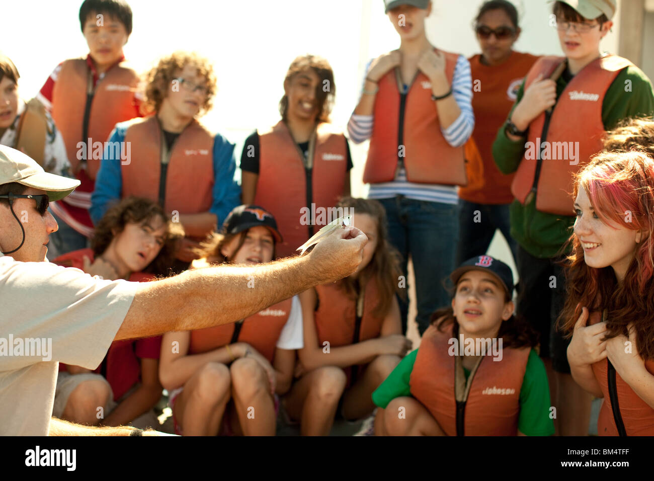 L'istruttore mostra piccoli pesci agli studenti delle scuole medie che indossano giubbotti di salvataggio arancioni durante una gita scolastica in biologia marina. ©Bob Daemmrich Foto Stock