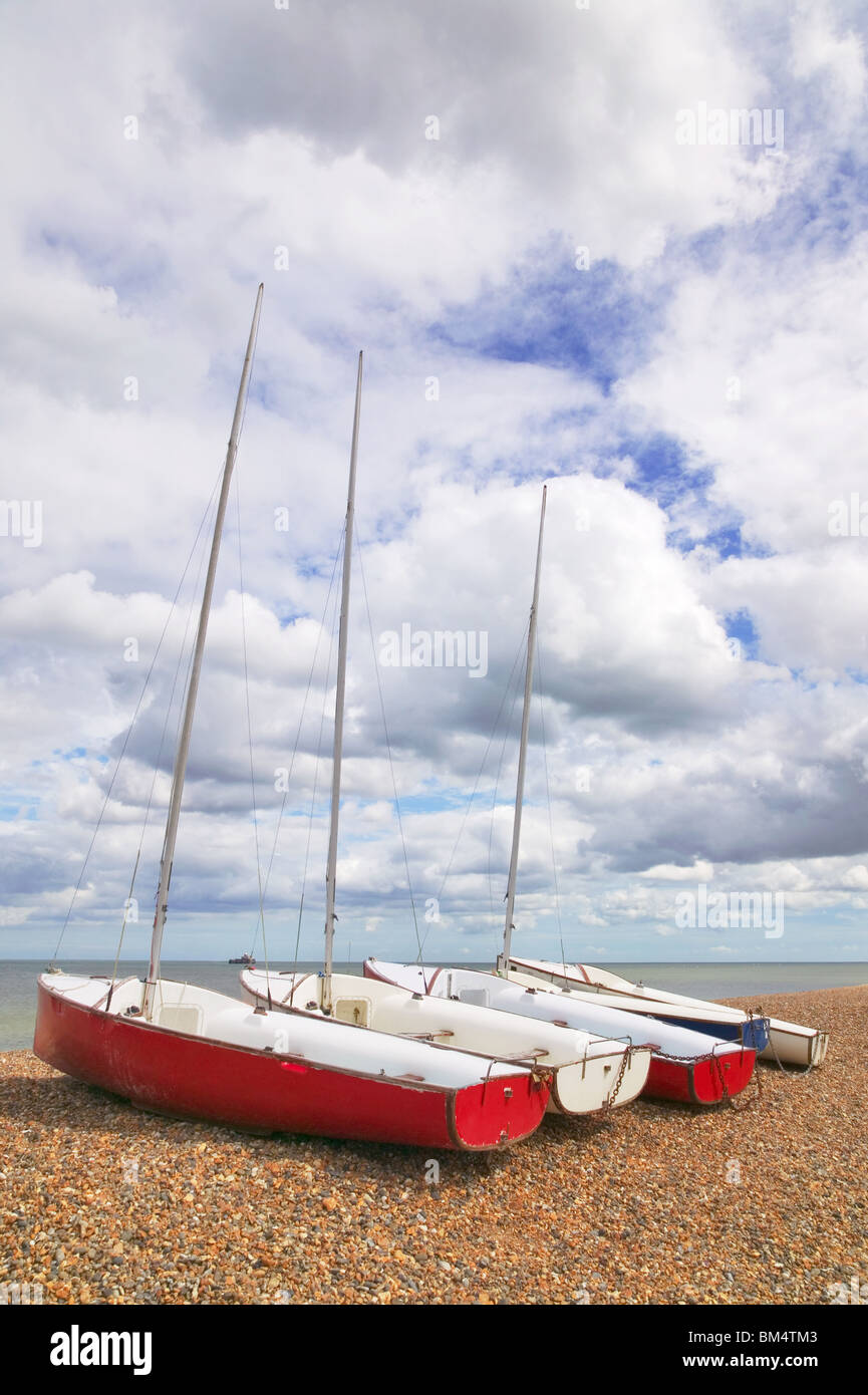 Quattro barche a vela allineati su di una spiaggia di ciottoli in una giornata di sole con blu cielo nuvoloso. Foto Stock