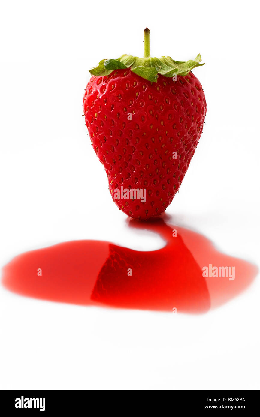 Una fragola su alcuni liquido rosso davanti a uno sfondo bianco Foto Stock