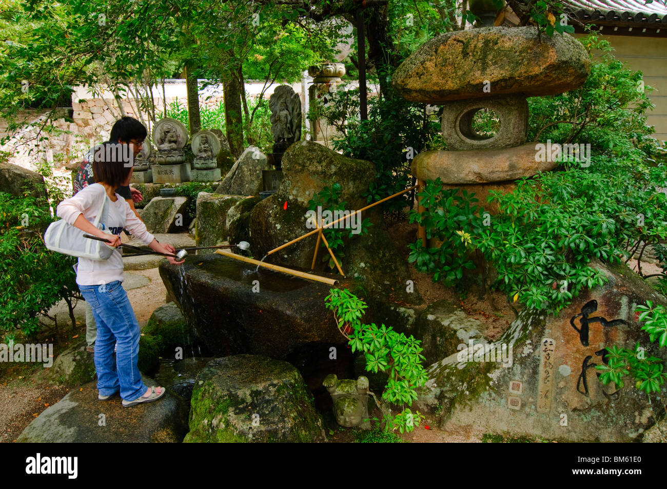 I visitatori di detergere le mani in una fontana di purificazione, Daisho-nel tempio, Miyajima, Honshu, Giappone Foto Stock