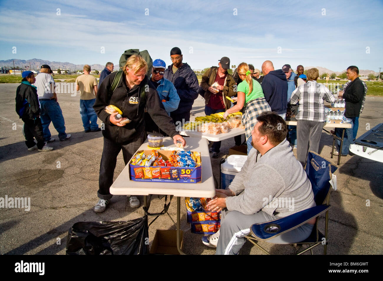 Senzatetto uomini line up per cibo gratuito fornito da una Chiesa locale in un lotto vacante in North Las Vegas, Nevada. Nota serve volontario Foto Stock