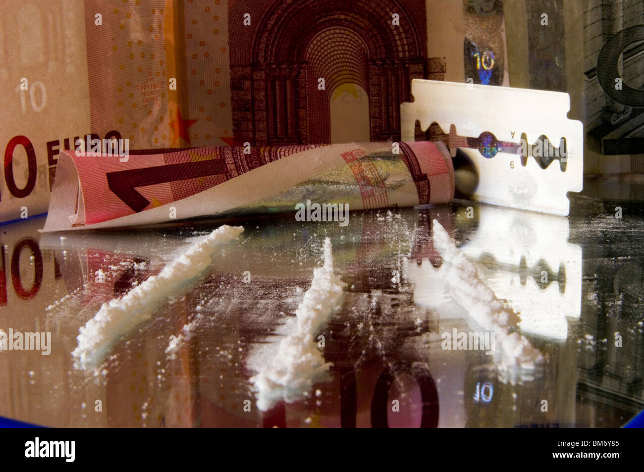 Close-up mostra piste di cocaina che convergono verso una banca laminato nota e la lama di un rasoio con sottofondo di euro Foto Stock