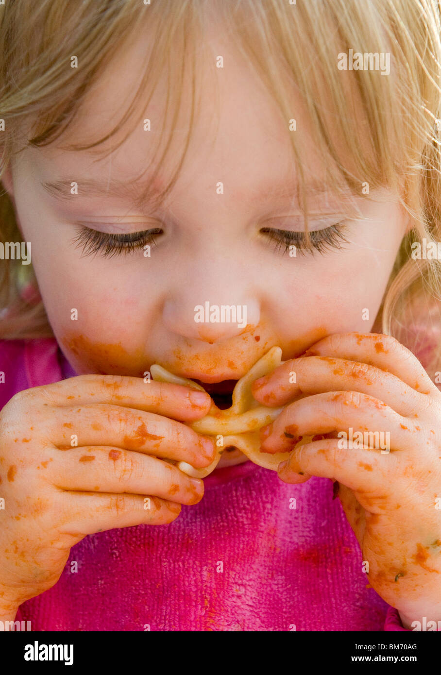 Ragazza TODDLER, gode di ottenere confuso mentre mangi la pasta in salsa di pomodoro Foto Stock