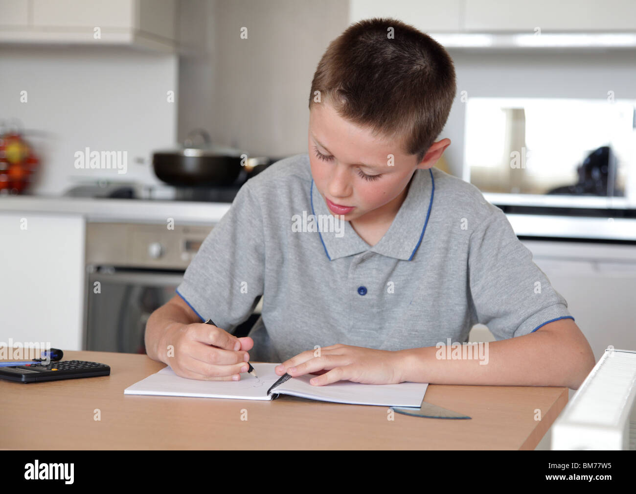 Ragazzo giovane facendo i compiti sul tavolo da cucina Foto Stock