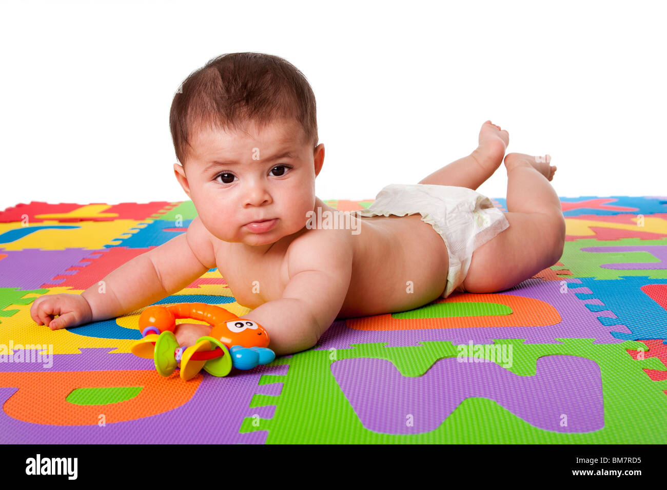 Bella carino felice ispanica caucasica baby recante sulla pancia in un colorato pavimento imbottito di piastrelle con alfabeto lettere e un giocattolo. Foto Stock