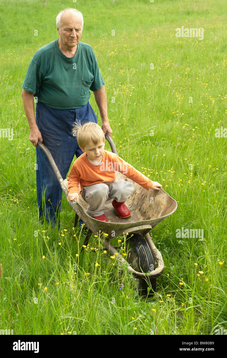 Nonno ragazzo di spinta nella ruota barrow in giardino Foto Stock