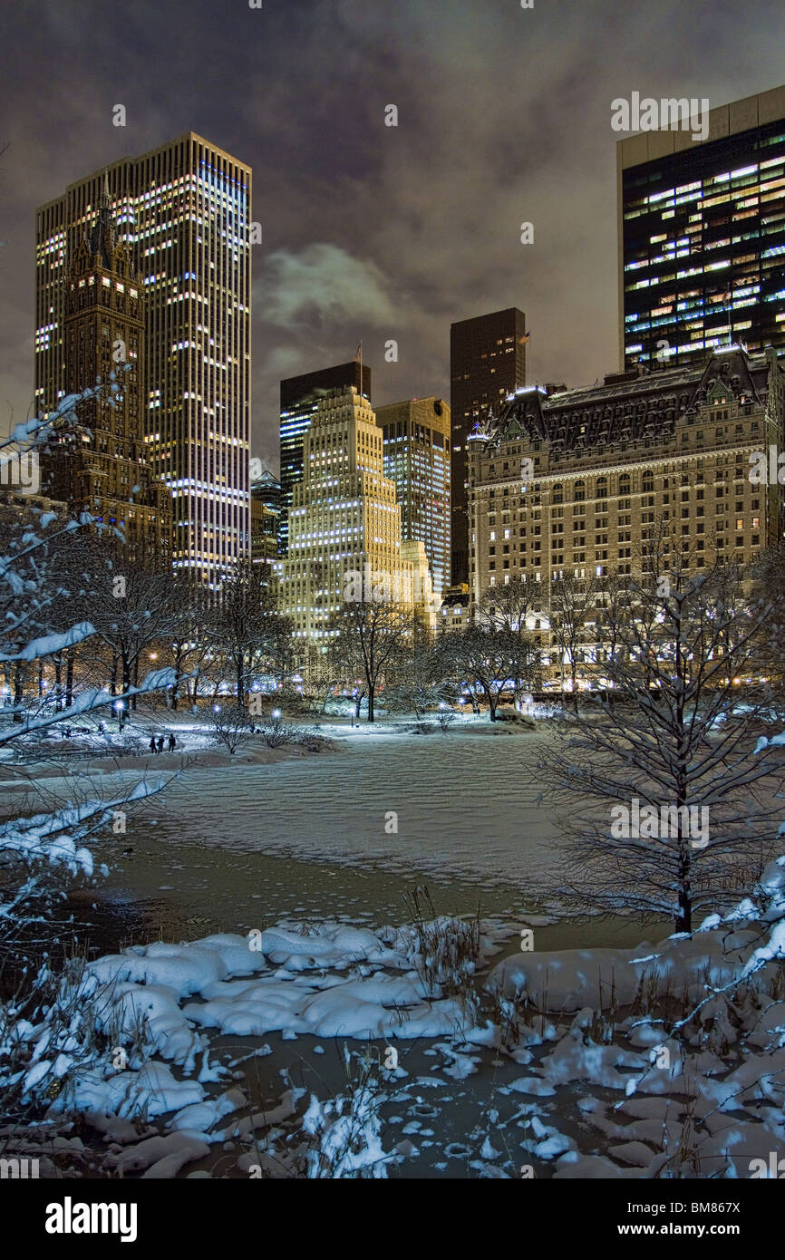 Skyline di Manhattan tra cui il Plaza Hotel & GM edificio a notte come visto da Gapstow Bridge in Central Park dopo una tempesta di neve Foto Stock