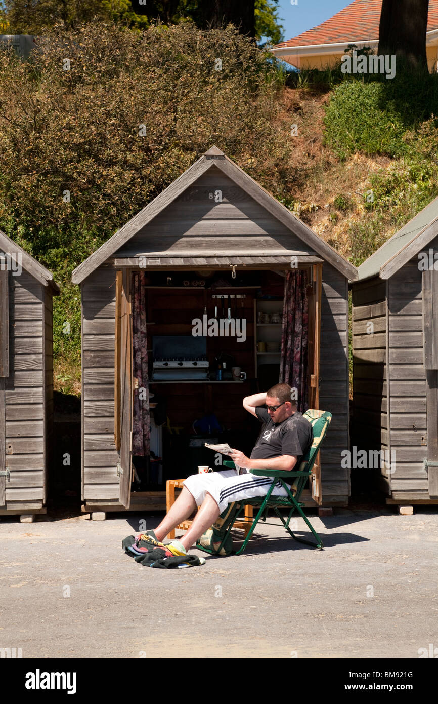 Uomo in sun sedia carta di lettura esterno aperto beach hut Foto Stock
