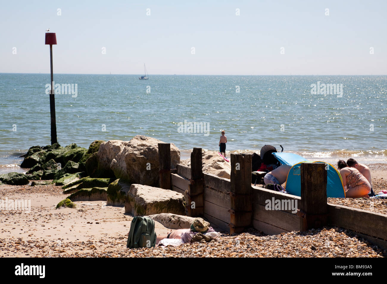 In legno e pietra con groyne polo del marcatore e cerca di sole sulla spiaggia a Mudeford Foto Stock