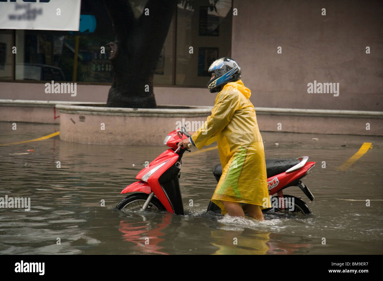 Moto Rider passeggiate la sua moto attraverso strade allagate durante il tifone stagione Foto Stock