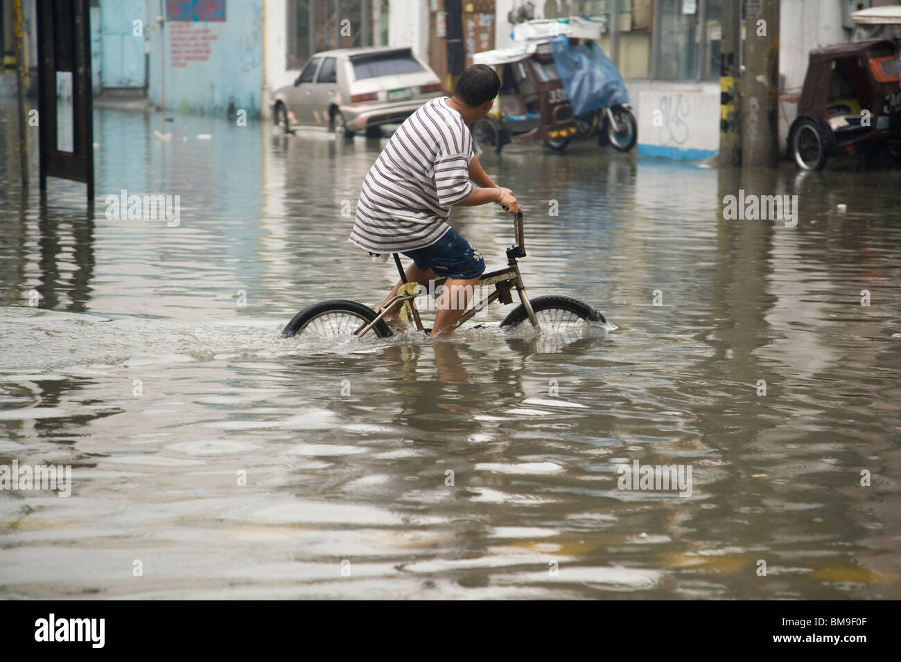 Un ciclista a prendere il suo moto su strade allagate durante il tifone stagione Foto Stock