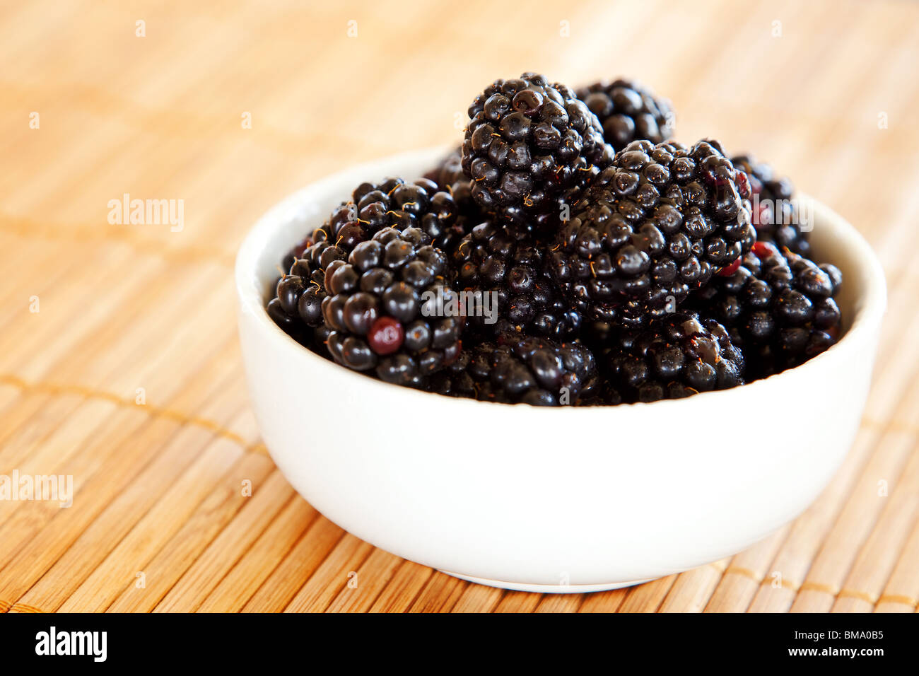 More in un bianco vaso in ceramica su un marrone di bambù sfondo mat Foto Stock