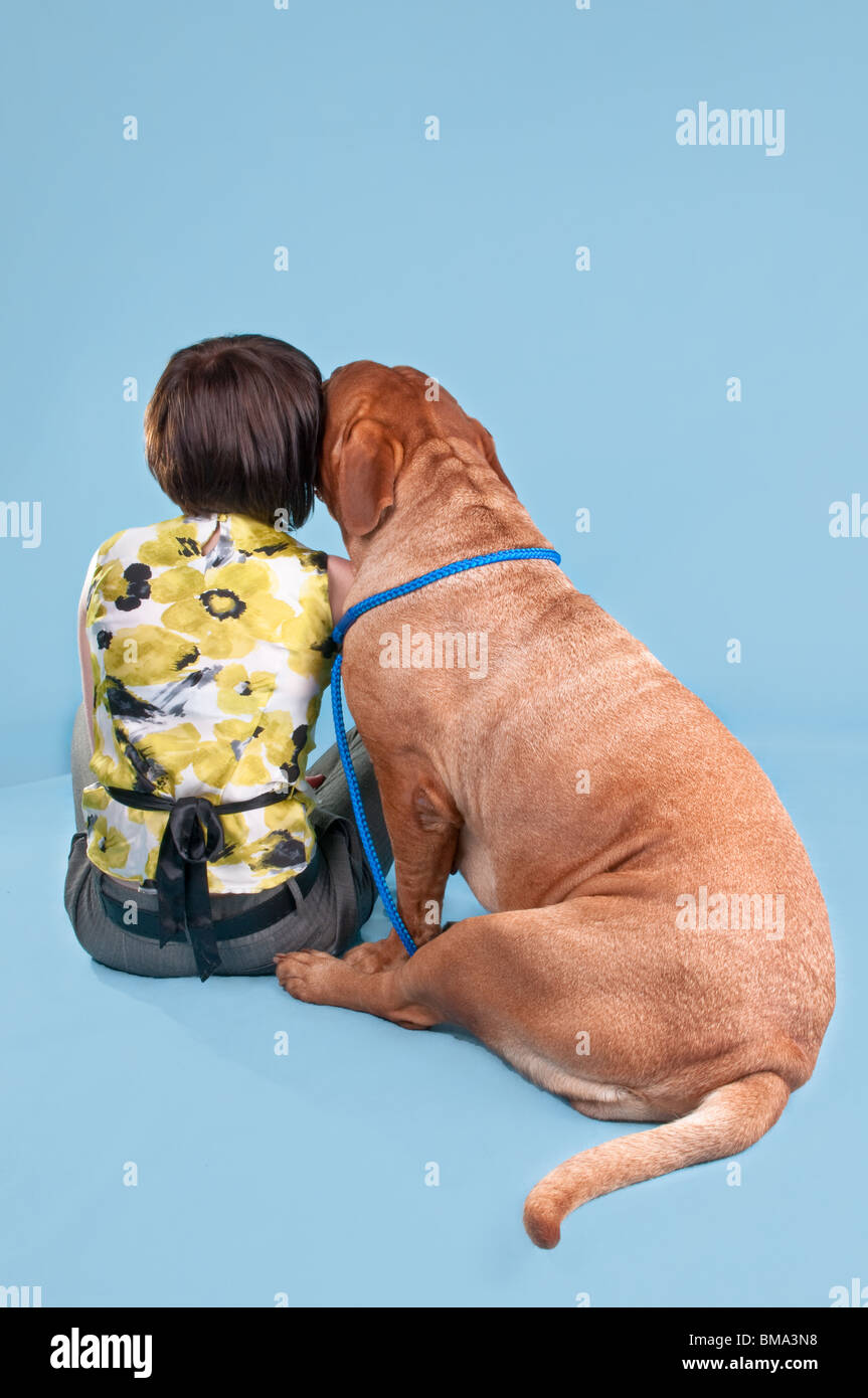 La ragazza e il suo cane de bordeaux seduti con la schiena rivolta verso la telecamera Foto Stock